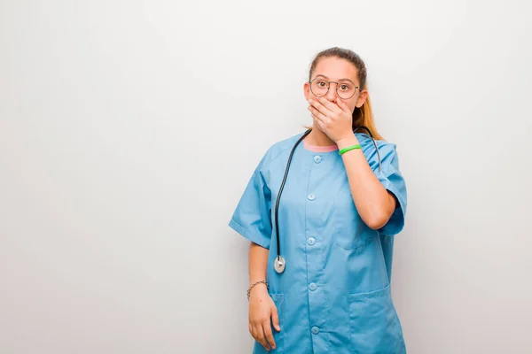 手で口を覆う若いラテン語の看護師はショックを受け驚きの表情を見せ秘密を守り白い壁に向かって誓いを立てる — ストック写真