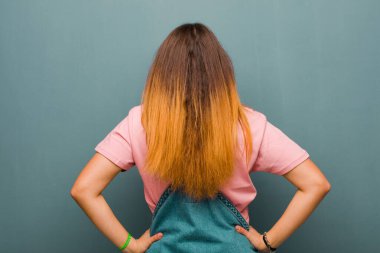 Genç, güzel, Latin bir kadın kafası karışık ya da dolu ya da şüphe ve soru dolu, merak ediyor, elleri kalçasında, dikiz aynasıyla grunge duvarına bakıyor.