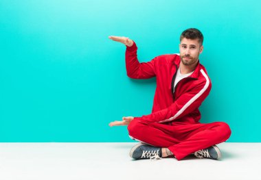 Genç bir handosme adamı iki eliyle bir objeyi tutuyor fotokopi alanında, düz renkli duvara karşı bir nesneyi gösteriyor, sunuyor ya da reklamını yapıyor.