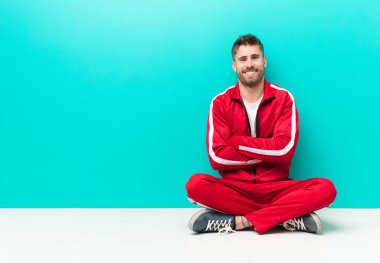 Genç adam mutlu, gururlu ve tatmin olmuş görünüyor. Kolları düz duvara çarpmış ve gülümsüyor.