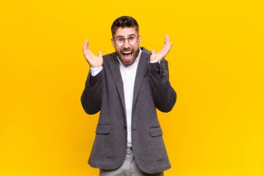 Genç adam şok olmuş ve heyecanlı, gülüyor, şaşırmış ve mutlu çünkü düz renkli duvara karşı beklenmedik bir sürpriz var.