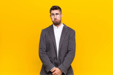 Genç adam şapşal ve komik görünüyor, şaşı bir ifadeyle, şaka yapıyor ve düz renkli duvarın etrafında takılıyor.