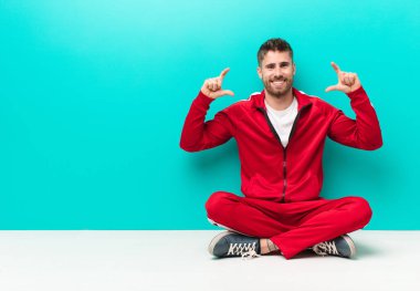 Genç adam kendi gülümsemesini çerçeveletiyor ya da özetliyor, iki eliyle, pozitif ve mutlu görünüyor, düz renkli duvara karşı sağIık kavramı