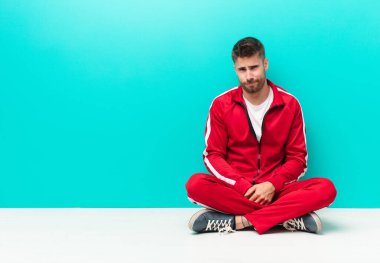 Genç adam gururlu, kendinden emin, havalı, küstah ve küstah görünüyor, gülümsüyor, düz renkli duvara karşı başarılı hissediyor.