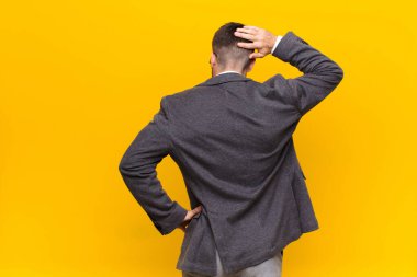 Genç Handome 'un kafası karışık ve bihaber, bir çözüm düşünüyor, eli kalçasında, diğeri kafasında, düz renk duvarına karşı dikiz manzaralı