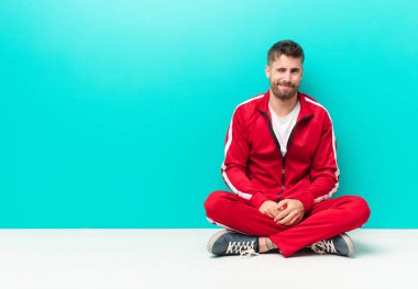 Genç adam mutlu ve arkadaş canlısı görünüyor. Düz renkli duvara karşı olumlu bir tavırla sana gülümsüyor ve göz kırpıyor.