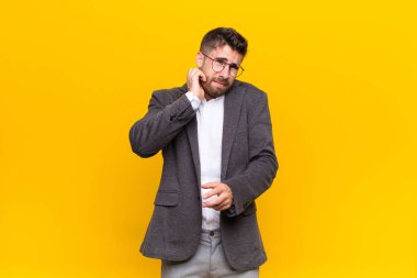 Genç adam stresli, hayal kırıklığına uğramış ve yorgun hissediyor, boynu ağrıyor, endişeli, sorunlu bir bakışla düz renkli duvara bakıyor.