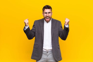 Genç adam kendini mutlu, pozitif ve başarılı hissediyor, zaferi kutluyor, başarıları kutluyor ya da düz renkli duvara karşı iyi şanslar diliyor.