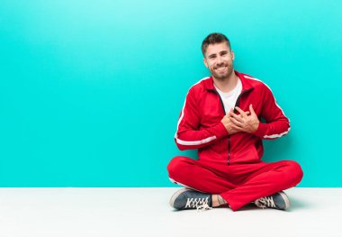 Genç adam romantik, mutlu ve aşık, neşeyle gülümseyen ve düz renkli duvara karşı kalbe yakın el ele tutuşan