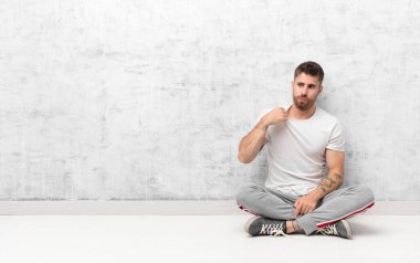 Genç adam kendini stresli, endişeli, yorgun ve hayal kırıklığına uğramış hissediyor, gömlek yakasını çekiyor, düz renkli duvara karşı sorunlu görünüyor.