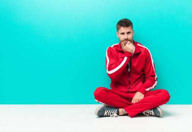 Genç adam ciddi görünüyor, kafası karışık, kararsız ve düşünceli, seçenekler arasında şüpheci veya düz renkli duvara karşı seçenekler