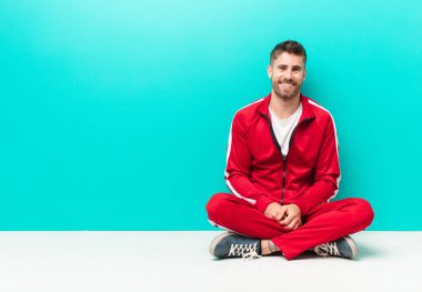 Genç adam mutlu ve hoş bir şekilde şaşırmış görünüyor, düz renkli duvara karşı büyüleyici ve şok olmuş bir ifadeyle heyecanlanıyor.