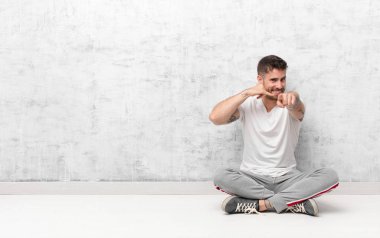 Genç Handome neşeyle gülümseyen ve kamerayı işaret eden adam daha sonra bir arama yaparken düz renkli duvara karşı telefonla konuşuyor.