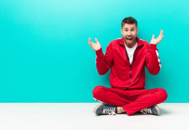 Genç adam şok olmuş ve heyecanlı, gülüyor, şaşırmış ve mutlu çünkü düz renkli duvara karşı beklenmedik bir sürpriz var.