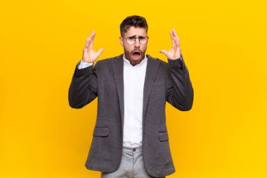 Genç adam elleri havada bağırıyor, öfkeli, sinirli, stresli ve düz renkli duvara karşı üzgün.