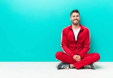 Genç adam mutlu ve şapşal görünüyor. Geniş, eğlenceli, kaçık bir gülüşü ve düz renkli duvarları olan gözleri var.