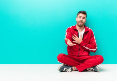 Genç adam mutlu ve aşık hissediyor, bir eli kalbinin yanında gülümsüyor ve diğeri düz renkli duvara doğru uzanıyor.