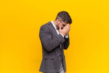 Hüzünlü, hayal kırıklığına uğramış bir bakışla gözlerini kapayan genç bir adam. Ağlıyor, düz bir duvara yan bakıyor.