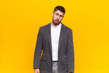 Genç handosme adam şaşkın ve şaşkın hissediyor, aptal, sersemlemiş bir yüz ifadesiyle düz renkli duvara karşı beklenmedik bir şeye bakıyor.