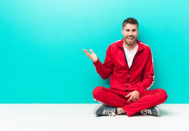 Genç adam kendini mutlu, şaşırmış ve neşeli hissediyor, olumlu bir tavırla gülümsüyor, düz renkli duvara karşı bir çözüm ya da fikir buluyor.