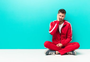 Yanak tutan ve ağrılı diş ağrısı çeken genç bir adam, hasta, sefil ve mutsuz hisseden, düz renkli duvara karşı bir dişçi arayan