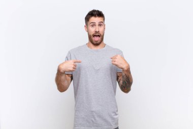 Genç adam kendini mutlu, şaşırmış ve gururlu hissediyor. Heyecanlı ve şaşkın bir bakışla düz renkli duvara bakıyor.