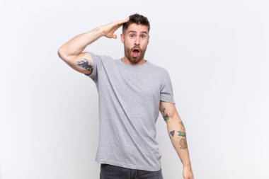 Genç adam mutlu, şaşkın ve şaşırmış görünüyor, gülümsüyor ve düz renkli duvara karşı inanılmaz ve inanılmaz iyi haberler veriyor.