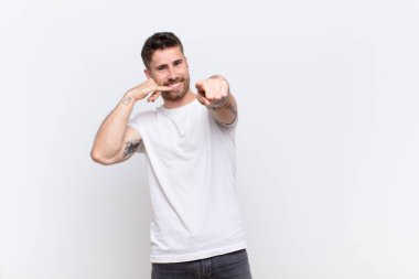 Genç Handome neşeyle gülümseyen ve kamerayı işaret eden adam daha sonra bir arama yaparken düz renkli duvara karşı telefonla konuşuyor.