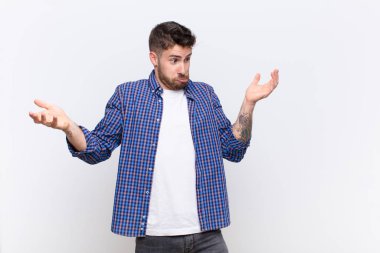 Genç adam aptal, çılgın, kafası karışık, kafası karışmış bir ifadeyle omuz silkiyor. Sinirli ve düz renkli duvara karşı cahil hissediyor.