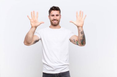 Genç adam gülümsüyor ve arkadaş canlısı görünüyor, onuncu ya da onuncu numarayı gösteriyor, düz renkli duvara doğru sayıyor.