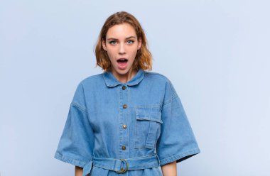 Genç sarışın kadın şok olmuş ya da şaşırmış görünüyor, ağzı açık bir şekilde düz duvara karşı 