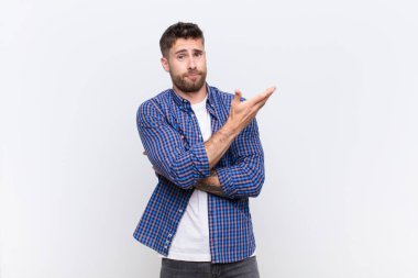 Genç adam kafası karışık ve cahil hissediyor, şüpheli bir açıklamayı merak ediyor ya da düz renkli bir duvara karşı düşünüyor.