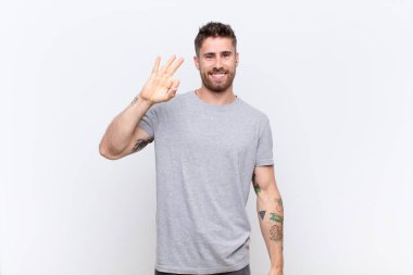 Genç adam kendini mutlu, rahat ve tatmin olmuş hissediyor. Onayını iyi bir hareketle gösteriyor. Renk duvarına gülümsüyor.