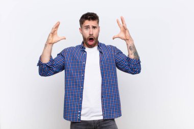 Genç adam elleri havada bağırıyor, öfkeli, sinirli, stresli ve düz renkli duvara karşı üzgün.