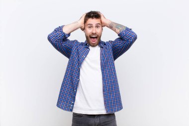 Genç handome adam el ele tutuşuyor, ağzı açık, son derece şanslı, şaşırmış, heyecanlı ve mutlu hissediyor düz renkli duvara karşı