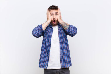Genç handosme adam mutsuz, korkmuş ya da endişeli görünüyor, ağzı sonuna kadar açık ve iki kulağı da düz renkli duvara karşı kapatıyor.