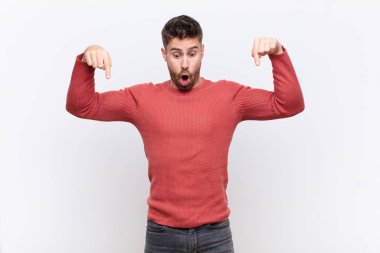 Genç adam şok olmuş, ağzı açık ve şaşırmış hissediyor. İnançsızlıkla bakıyor ve şaşırıyor ve düz renk duvara karşı şaşırıyor.