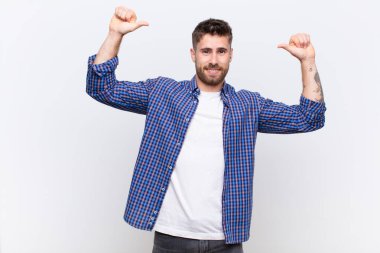 Genç adam kendini gururlu, kibirli ve kendinden emin hissediyor. Tatmin olmuş ve başarılı görünüyor. Düz renkli duvara işaret ediyor.