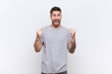 Genç adam şok olmuş, heyecanlı ve mutlu hissediyor, gülüyor ve başarıyı kutluyor, vay canına! yassı renk duvarına karşı