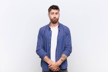 Genç adam şapşal ve komik görünüyor, şaşı bir ifadeyle, şaka yapıyor ve düz renkli duvarın etrafında takılıyor.