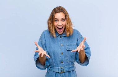 Genç sarışın kadın kendini mutlu, şaşkın, şanslı ve şaşırmış hissediyor. Düz renkli duvara karşı inanılmaz.