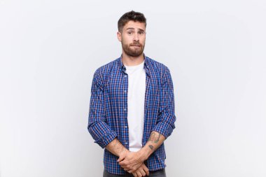 Genç adam şaşkın ve şaşkın görünüyor, gergin bir hareketle dudağını ısırıyor, düz renk duvarına karşı sorunun cevabını bilmiyor.