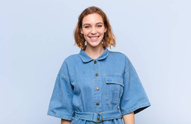 Genç sarışın kadın mutlu ve şapşal görünüyor. Geniş, eğlenceli, kaçık bir gülüşü ve düz renkli duvarları olan gözleri var.