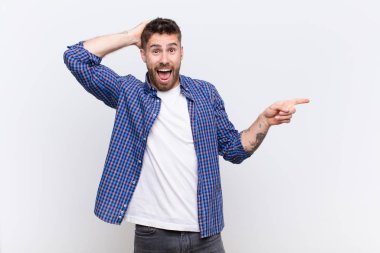 Genç adam gülüyor, mutlu, pozitif ve şaşırmış görünüyor, düz renkli duvara karşı yanal fotokopi alanını gösteren harika bir fikrin farkına varıyor.