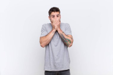 Genç adam mutlu, neşeli, şanslı ve şaşırmış görünüyor. İki elini de düz duvara dayayıp ağzını kapatıyor.