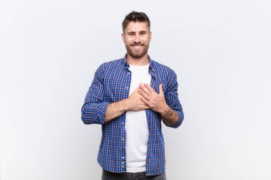 Genç adam romantik, mutlu ve aşık, neşeyle gülümseyen ve düz renkli duvara karşı kalbe yakın el ele tutuşan