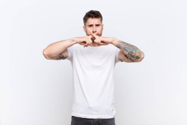 Genç adam ciddi görünüyor ve reddedilmek için iki parmağının önde olması hoşnutsuz, düz renkli duvara karşı sessizlik istiyor.