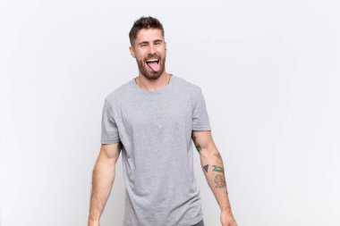 Neşeli, kaygısız, asi tavırlı, şakacı ve dilsiz genç bir adam, düz renkli duvara karşı eğleniyor.