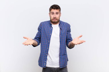 Genç Handome 'un kafası karışık ve bihaber, hangi seçeneği seçeceğinden emin değil, düz renkli duvara karşı merak içinde.