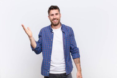 Genç adam kendini mutlu, şaşırmış ve neşeli hissediyor, olumlu bir tavırla gülümsüyor, düz renkli duvara karşı bir çözüm ya da fikir buluyor.